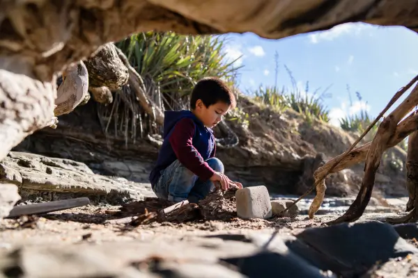 Criança participando de brincadeiras criativas ao montar um abrigo natural com galhos e folhas, desenvolvendo habilidades de imaginação, colaboração e conexão com a natureza.