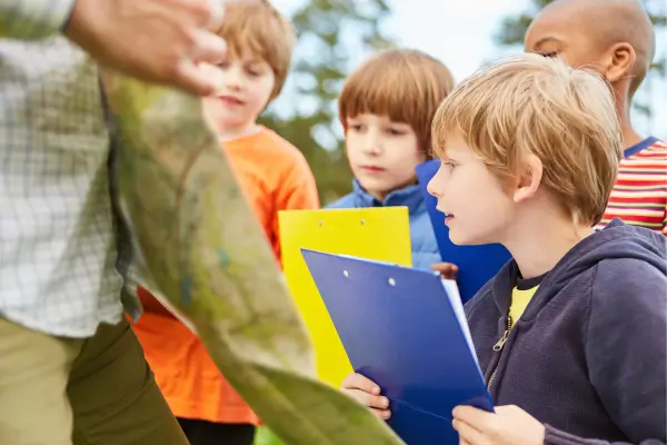 Crianças criando um diário da natureza, registrando o que observam ao ar livre com desenhos e anotações, desenvolvendo a atenção aos detalhes e a conexão com o ambiente natural.