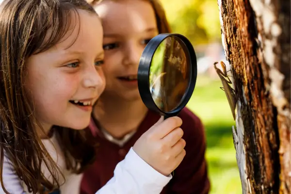 Crianças realizando experimentos de observação, usando uma lupa para explorar de perto o comportamento e as características de pequenos insetos no jardim.