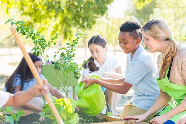 Crianças regam plantas juntas em um jardim, colaborando e se comunicando entre si, como exemplo dos benefícios das brincadeiras que desenvolvem habilidades sociais na infância.