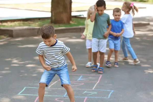 Crianças se divertindo brincando de amarelinha, pulando entre os quadrados desenhados no chão e desenvolvendo coordenação, equilíbrio e muita alegria ao ar livre.