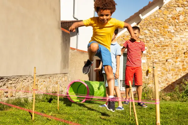 Crianças participando de brincadeiras ao ar livre, pulando obstáculos com entusiasmo e energia, estimulando o movimento, a coordenação motora e a diversão em grupo.