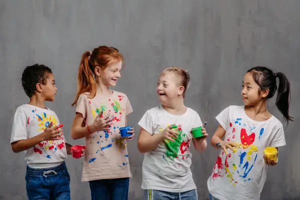 Crianças se divertindo com brincadeiras de pintura, cobertas de tintas coloridas, expressando criatividade e alegria em uma atividade artística ao ar livre.