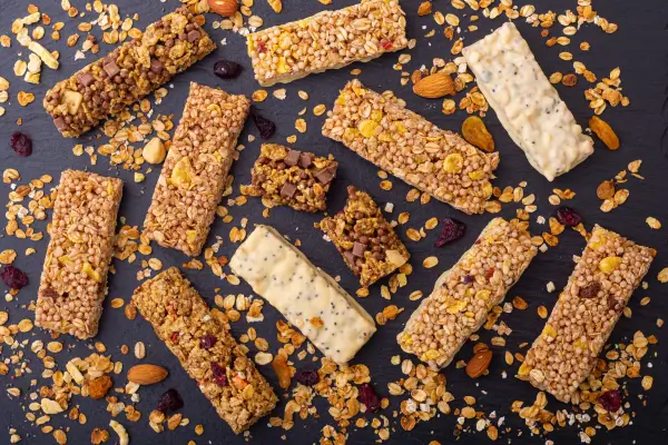 Barrinhas de cereais feitas em casa, rodeadas de frutas secas e castanhas, perfeitas para lanches saudáveis dos pequenos
