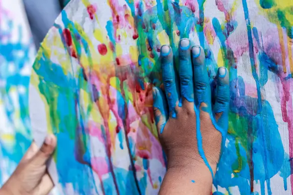 Mão infantil espalhando terra em uma pintura, explorando texturas e cores com elementos naturais de forma criativa.