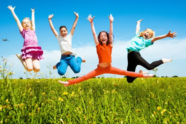 Crianças pulando alegremente ao ar livre durante atividades criativas, representando momentos de diversão e aprendizado em projetos lúdicos com a natureza.
