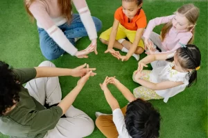 Crianças sentadas em um espaço ao ar livre aguardam animadas o início de uma gincana, em um momento de expectativa e preparação para atividades em grupo cheias de movimento e diversão