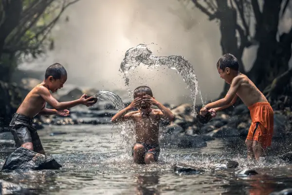 Três meninos brincando na água ao ar livre, explorando de forma divertida elementos do ciclo da água.