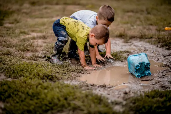 Crianças se divertindo com as mãos e os pés na lama, em contato direto com elementos naturais como terra e água.