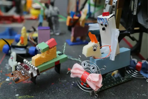 Brinquedos feitos com materiais reciclados, como carrinhos de garrafa PET, bonecos de rolo de papelão e aviões de tampinhas, expostos sobre uma mesa, mostrando como a reciclagem pode se transformar em