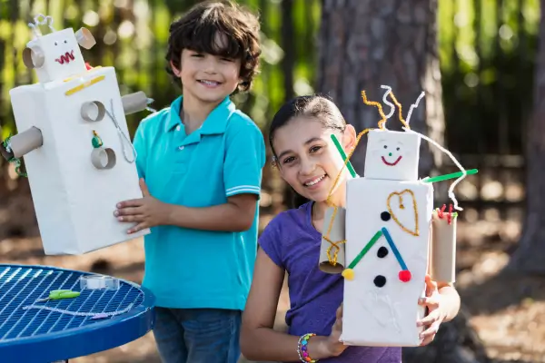 Duas crianças brincam com bonecos feitos com materiais recicláveis, como rolos de papel e tampinhas, em uma atividade criativa e ecológica que estimula a reutilização e o cuidado com o meio ambiente.