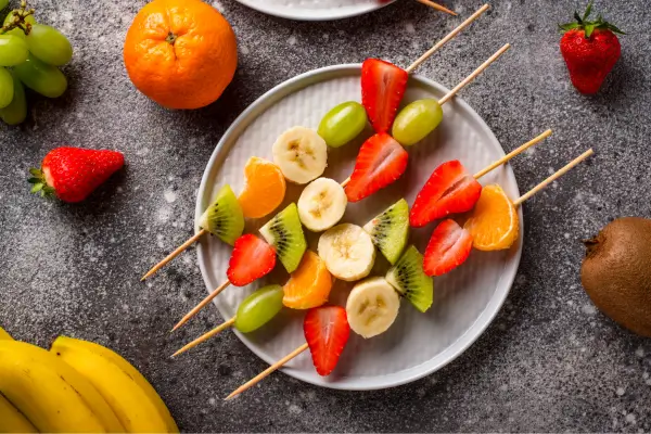 Prato colorido com espetinhos de frutas frescas, combinando sabores e cores vibrantes.