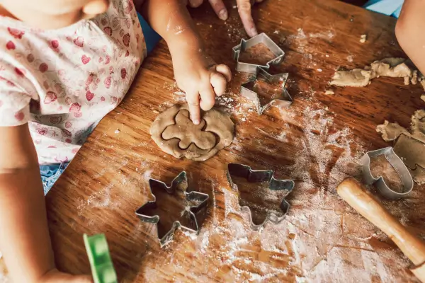 Criança em atividade infantil preparando biscoitos de gengibre com formas divertidas em uma mesa de cozinha, promovendo aprendizado e criatividade através da culinária.