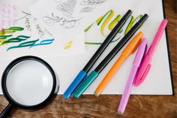 Materiais para um diário de exploração: canetas coloridas, papéis e uma lupa sobre a mesa, prontos para registrar descobertas e aventuras ao ar livre.