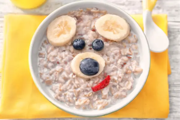 Tigela de mingau de aveia decorada com frutas formando o rosto de um urso, criando uma refeição divertida e nutritiva."