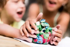 Crianças modelando barro com as mãos em uma atividade ao ar livre, vivenciando a criatividade e a expressão tátil em um estúdio de arte natural e sensorial