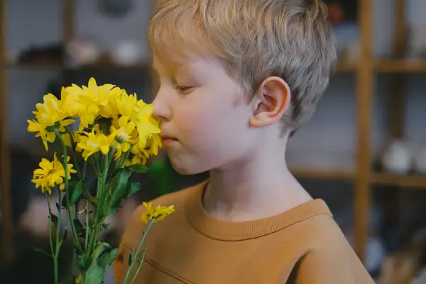 Criança cheira flores em um ambiente ao ar livre, explorando aromas da natureza como parte de atividades sensoriais que estimulam o olfato e promovem a conexão com o meio ambiente.