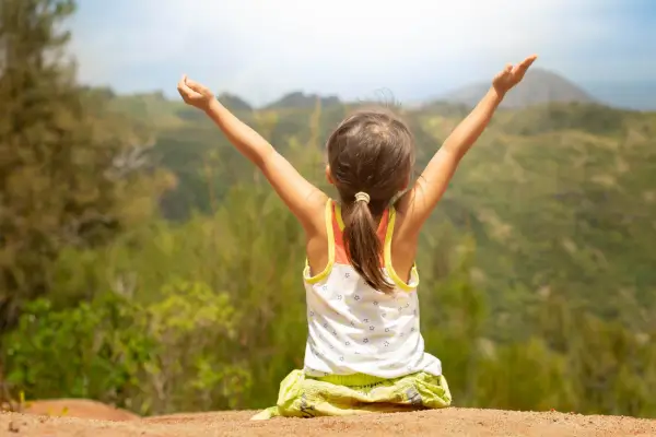 Criança sentada em uma pedra observa o ambiente ao redor e escuta atentamente os sons da natureza, em um momento de contemplação ao ar livre.