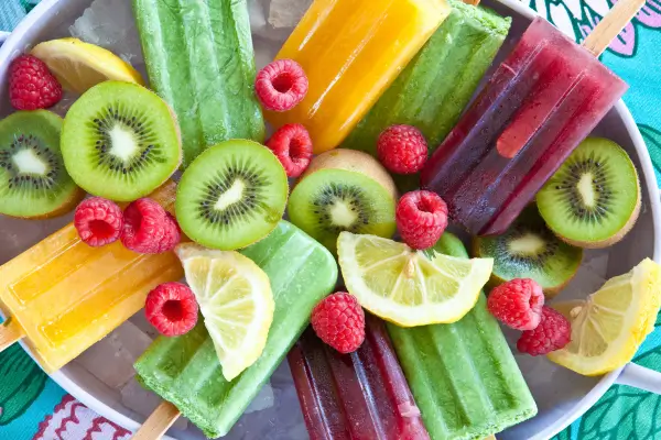 Picolés caseiros feitos com frutas naturais, servidos ao lado de uma tigela com frutas frescas, em uma atividade de culinária saudável para crianças.