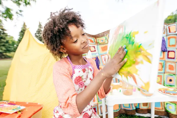 Menina pintando com tintas naturais feitas de frutas e vegetais, explorando cores e texturas em uma atividade de arte ao ar livre que estimula a criatividade e o contato com a natureza.