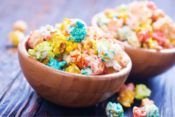 Duas tigelinhas com pipocas coloridas dispostas sobre uma mesa, em uma apresentação criativa e divertida que transforma um lanche simples em uma experiência visualmente encantadora.
