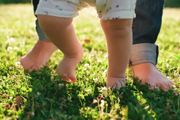 Pai e bebê caminham descalços na grama, compartilhando um momento de conexão e descobertas táteis, como exemplo dos benefícios do contato com a natureza para o desenvolvimento sensorial na primeira infância