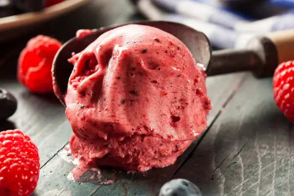 Bola de sorvete feito com frutas congeladas servida ao lado de frutas vermelhas frescas, representando uma sobremesa criativa, saudável e colorida.