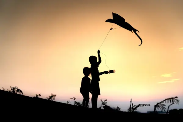 Crianças soltando pipa ao anoitecer durante atividades ao ar livre, aproveitando a liberdade e a magia do céu aberto.