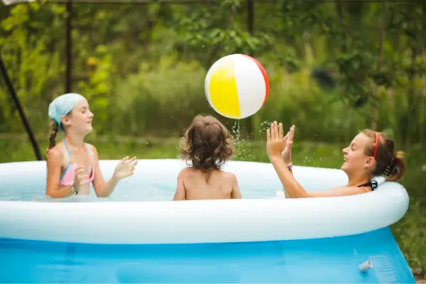 Crianças sentadas em uma piscina inflável no quintal, brincando com bola